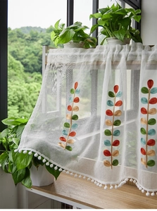 Detail of white sheer café curtain featuring colorful leaf embroidery and pom-pom trim