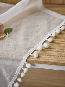 Detail of translucent polyester curtain with white pompom trim and floral embroidery