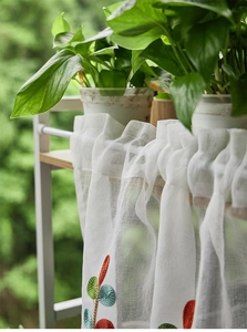 Detail of white sheer curtain with colorful leaf embroidery on lightweight polyester fabric