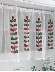Dettaglio della tenda da caffè bianca con ricami a foglia colorati e bordo a pompon
