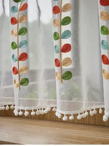 Detail of white sheer curtain with colorful leaf embroidery and white pom-pom fringe trim