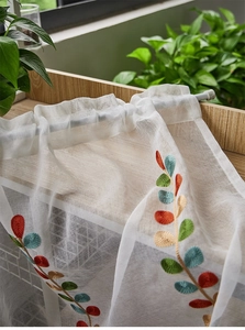 Detailed view of white sheer curtain with colorful leaf embroidery on textured fabric
