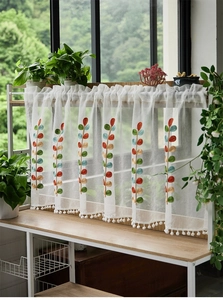 Detailed embroidery of colored leaves and white pom-pom trim on a sheer cafe curtain