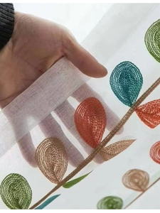 Dettaglio di tenda velata bianca semitrasparente con ricamo a forma di foglie colorate