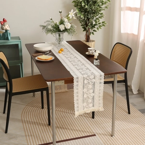 White vintage lace table runner with floral crochet pattern and tassels on wooden table