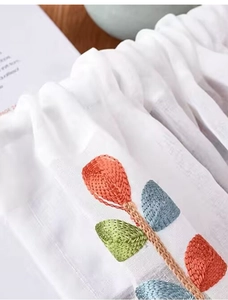 Dettaglio di tessuto bianco semitrasparente con ricami colorati e balze elasticizzate