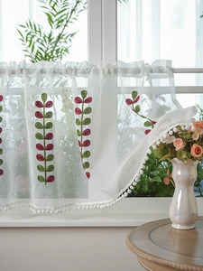 Detailed embroidery of red and green leaves on white semi-sheer cafe curtain with pom-poms