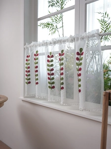 Close-up of white sheer cafe curtain with leaf embroidery and pom-pom trim detail