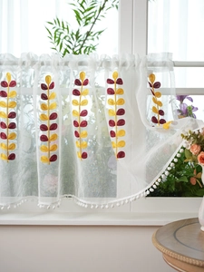 Detail of white semi-transparent sheer kitchen curtain with yellow embroidery and pom-poms