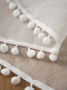 Close-up of white semi-transparent polyester cafe curtain with decorative pom-pom edges