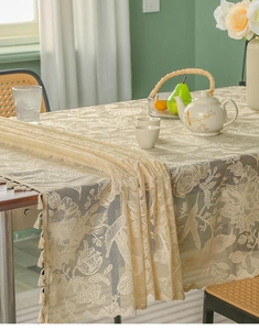 Close-up of elegant beige floral lace tablecloth with fringe tassels on a wooden table