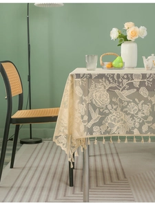 Detailed close-up of beige lace tablecloth with hummingbird floral jacquard and tassel edge