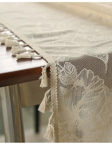 Detailed view of beige lace table runner with floral patterns and delicate tassels
