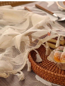 Close-up of cream lace tablecloth with diamond grid pattern and delicate tassel edge