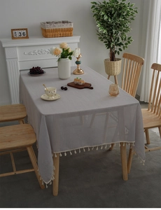 Detail of grey linen tablecloth with elegant cream fringe tassels on a wooden table