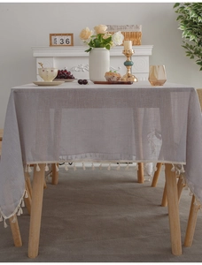 Close-up of linen-textured tablecloth with delicate cream fringe tassels on a wooden table