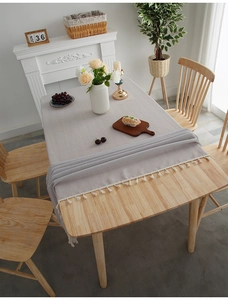 Close-up of light gray linen tablecloth with cream fringe on a wooden table