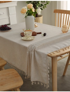 Close-up of linen-textured beige tablecloth with elegant fringe tassels on wooden table