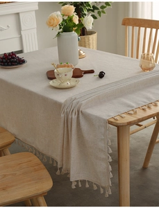 Close-up of beige linen tablecloth with handcrafted fringe detail on wooden table