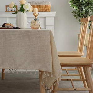 Linen texture rectangular tablecloth with cream fringe tassels on a solid wood dining table
