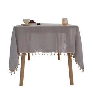 Linen cotton tablecloth with decorative cream tassels on light purple fabric surface