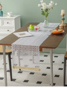 Detail of white hollowed-out lace table runner with geometric knit and yellow tassels