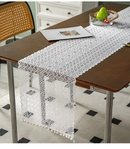 Macro shot of white geometric openwork lace runner with decorative pom-pom tassels