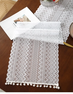 Close-up of white hollow knit table runner with pom-pom fringe on a dark wood table