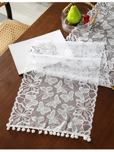 Detail showing white lace table runner with butterfly patterns and pom-pom edge trim