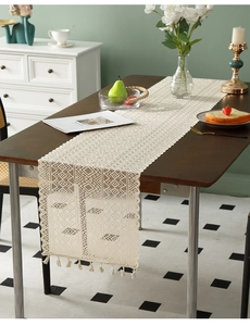 Detail of hollow geometric crochet table runner with tassels on dark wood table