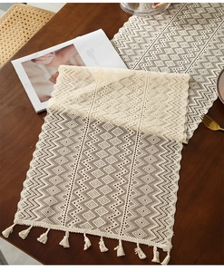 Close-up of beige crochet table runner with hollow geometric patterns and tassel edges