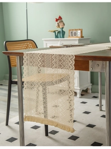 Close-up of beige crochet table runner with hollow geometric patterns and delicate fringe