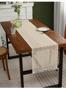 Detail of crochet table runner with hollow geometric patterns and white pom-pom fringe