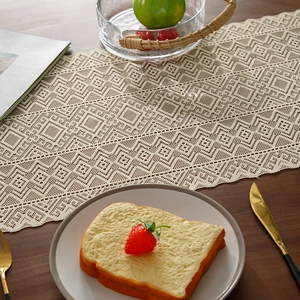 Elegant beige hollow crochet table runner with geometric patterns on dark wooden table