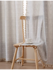 Close-up of light gray plaid linen curtain featuring decorative fringe tassels for home decor