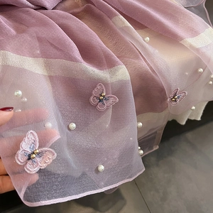 Détail de la broderie papillon avec perles dorées et nacrées sur une écharpe en soie mauve