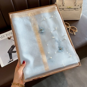 Détail d'une écharpe en soie bleu clair avec broderie papillon 3D et décorations de perles