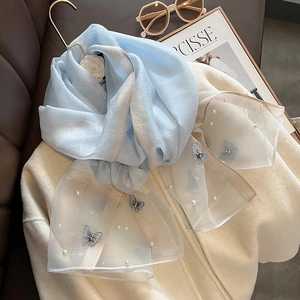 Détail de broderies papillon et petites perles sur une écharpe bleu clair en soie