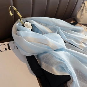 Gros plan sur foulard en soie bleu clair avec rayures métalliques argentées et bords roulés