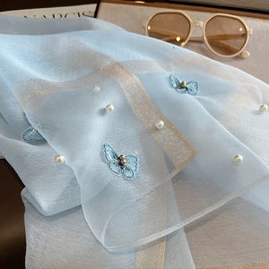 Détail de foulard en soie bleu clair avec broderie papillon, perles et bord doré