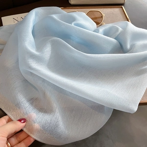 Écharpe en soie bleu clair translucide avec bordure scintillante sur un plateau