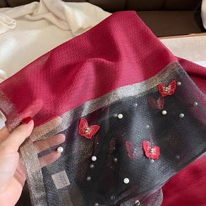 Détail de la broderie papillon rouge et perles blanches sur une écharpe en soie