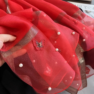 Détail d'une écharpe en soie rouge avec rayures dorées, perles et broderie papillon