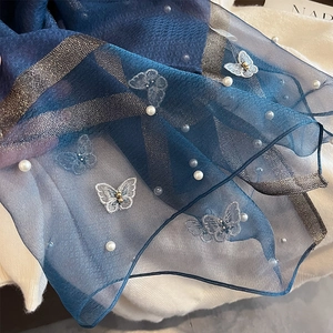 Détail d'une écharpe en soie bleue avec broderie papillon et perles délicates