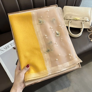 Détail de l'écharpe en soie jaune avec broderie papillon et perles dans un coffret cadeau