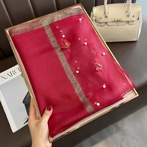 Détail d'un châle en soie rouge avec broderie papillon, perles blanches et bordure dorée