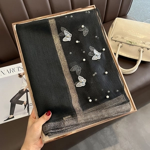 Détail d'une écharpe en soie noire avec broderie papillon, perles et bordure dorée