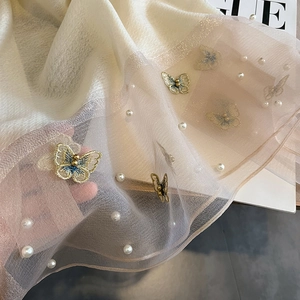 Détail d'une écharpe en soie crème avec broderie papillon et ornements de perles blanches