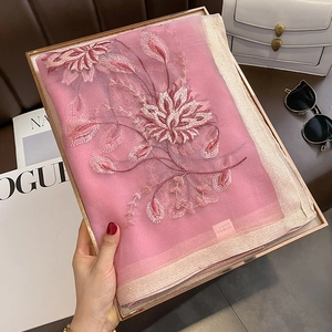Gros plan d'une écharpe en soie et laine rose avec broderie florale et bords scintillants