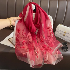 Détail d'une écharpe en soie et laine rouge avec broderie florale et fils dorés fins